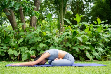 Bahçede yoga yapan genç bir kadının portresi. Yaşam tarzı uygunluğu ve sağlıklı olma kavramı. Asyalı kadınlar parkta yoga yapıyorlar..
