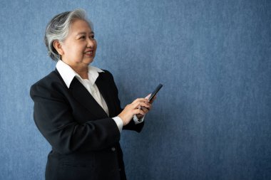 Portrait of middle aged business woman standing isolated on blue background and use smartphone for check finance, looking at the camera with smile, Successful businesswoman, ceo, director, manager