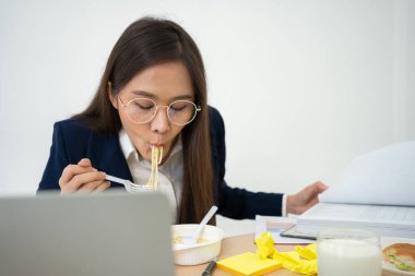 Busy and tired businesswoman eating spaghetti for lunch at the Desk office and working to deliver financial statements to a boss. Overworked and unhealthy for ready meals, burnout concept.