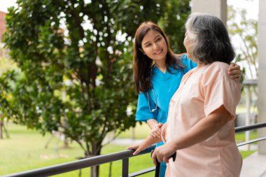 Asian careful caregiver or nurse hold patient hand and encourage patient, walking in garden. Concept of happy retirement with care from a caregiver and Savings and senior health insurance.