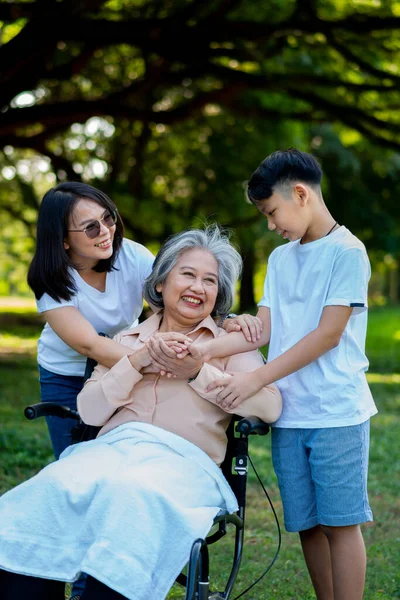 快乐的亚洲老奶奶带着她的女儿和孙子在公园里坐轮椅 孙子来看望老奶奶 牵着手 幸福家庭的概念 良好的关系 免版税图库图片