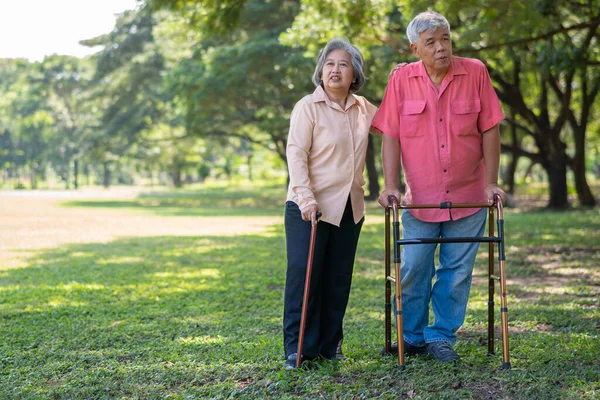 An old elderly Asian man uses a walker and walks in the park with his wife.  Concept of happy retirement With Love and care from family and caregiver, Savings, and senior health insurance