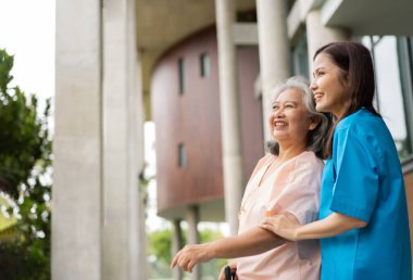 Asian careful caregiver or nurse hold patient hand and encourage patient, walking in garden. Concept of happy retirement with care from a caregiver and Savings and senior health insurance.