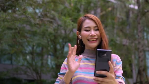 一个微笑的女游客在酒店的公园里通过短信链接聊天 开心点短信聊天 在户外用手机与快乐女人在网上聊天 — 图库视频影像