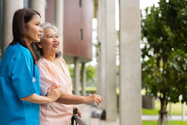 Asian careful caregiver or nurse hold patient hand and encourage patient, walking in garden. Concept of happy retirement with care from a caregiver and Savings and senior health insurance.