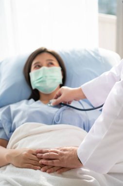 Asyalı kadın doktorlar hastanın elini tutar ve tıbbi tavsiyelerde bulunurken doktorlar da hastanın kalbini kontrol etmek için stetoskop kullanır. Şefkat ve şefkat kavramı
