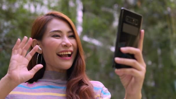一个微笑的女游客在酒店的公园里通过视频链接聊天 开心点视频聊天 在户外用手机拍下快乐女人在网上聊天的视频 — 图库视频影像