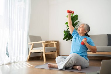 Asian senior woman lifting dumbbell for exercise and workout at home. Active mature woman doing stretching exercise in living room. Exercise Active and healthy for older, elder, and senior concept.