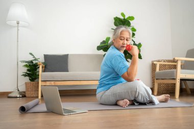 Asian senior woman lifting dumbbell for exercise and workout at home. Active mature woman doing stretching exercise in living room. Exercise Active and healthy for older, elder, and senior concept.