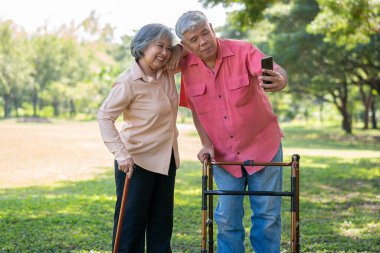 Yaşlı bir Asyalı, karısıyla fotoğraf çektirmek için Walker 'ı ve akıllı telefonu kullanıyor. Aile ve bakıcı, birikim ve sağlık sigortası ile mutlu emeklilik kavramı
