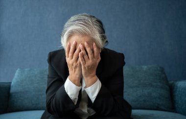 Başı ağrıyan yorgun, yaşlı bir kadın. Asyalı kıdemli iş kadını çok çalışmanın stresi. Hüsrana uğramış iş kadını, iş yerinde oturan, sıkıntılı hisseden, çaresiz görünen bir konsept düşünüyor.