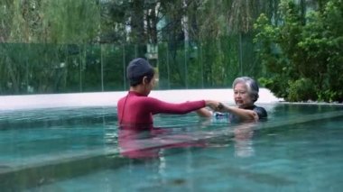 Young trainer helping senior woman in aqua aerobics and working out in the pool. old woman and mature man doing aqua aerobics exercise in swimming pool, Elderly sports, and active lifestyle concept.