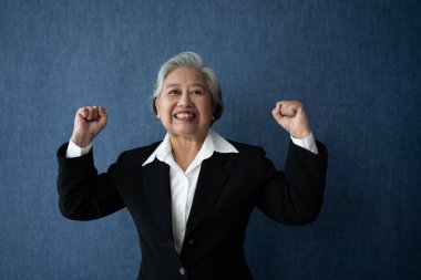 Portrait of middle aged business woman standing isolated on blue background and raise your arms to show success, looking at the camera with smile, Successful businesswoman, ceo, director, manager