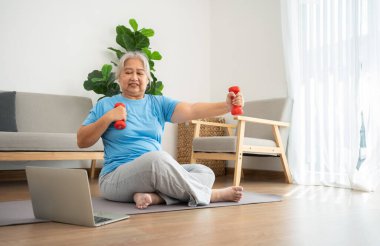 Asian senior woman lifting dumbbell for exercise and workout at home. Active mature woman doing stretching exercise in living room. Exercise Active and healthy for older, elder, and senior concept.