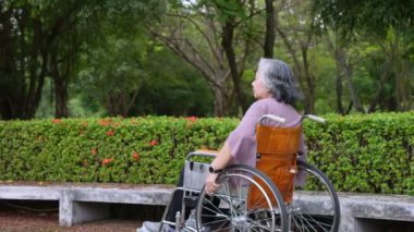 Happy alone Asian senior women sitting in wheelchair and pushing wheelchairs to move forward in the park, Concept of happy retirement with care from a caregiver and Savings and senior health insurance