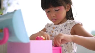 Küçük sevimli Asyalı kız çocuğu ağzını pembe çocuk kafalarıyla boyuyor ve aynaya bakıyor. Oyuncak güzellik salonunda bir çocuk oynuyor. Anaokulu öğrencilerinin öğrenme gelişimini arttır.