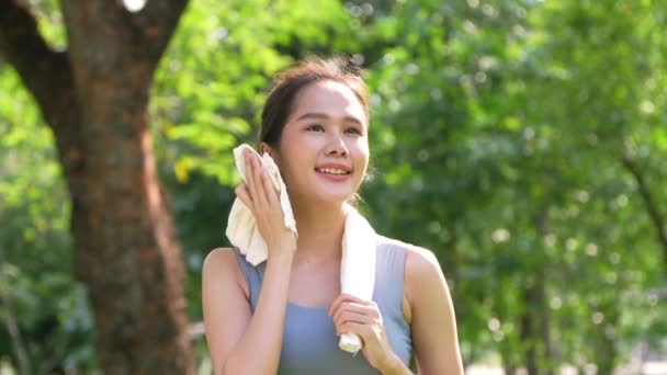 形象年轻的亚洲女人迷人的微笑和使用白色毛巾休息后 微笑着运动的年轻女子在室外锻炼 看着相机 健康的生活方式 — 图库视频影像