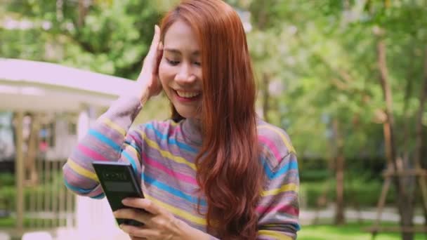 一个微笑的女游客在酒店的公园里通过短信链接聊天 开心点短信聊天 在户外用手机与快乐女人在网上聊天 — 图库视频影像