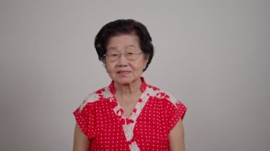 Neşeli gülümseyen Asyalı son sınıf öğrencisi kadın gözlük takıyor beyaz arka plan üzerine gri saçlar takıyor ve kazanan hareketi yaparken kollarını kaldırıp gülümsüyor ve başarı için bağırıyor. Kutlama