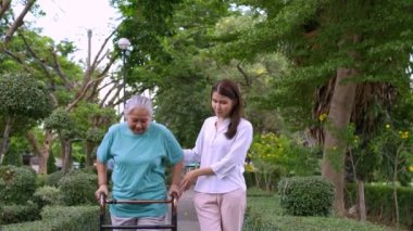 Yaşlı bir Asyalı kadın yürüteç kullanıyor ve kızıyla bahçede yürüyor. Mutlu emeklilik kavramı. Bakıcının, birikimin, sağlık sigortasının ve sağlık hizmetlerinin bakımıyla.