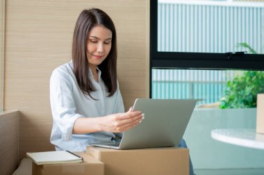 Mutlu Asyalı genç girişimci ev bilgisayarındaki bir dizüstü bilgisayardan siparişleri kontrol ettikten sonra satış başarısı için gülümseyin, İnternet ve e-ticaret ticaret sektörü kavramı