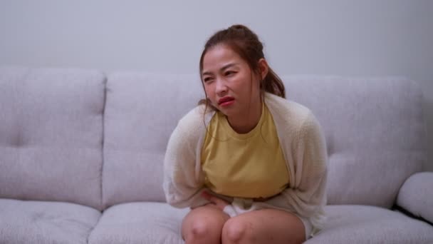 月経期間のために腹部の急性腹痛に苦しむアジアの女性 Pms ソファに座って 食中毒から胃の痛み 腹部の痛み 消化不良 — ストック動画