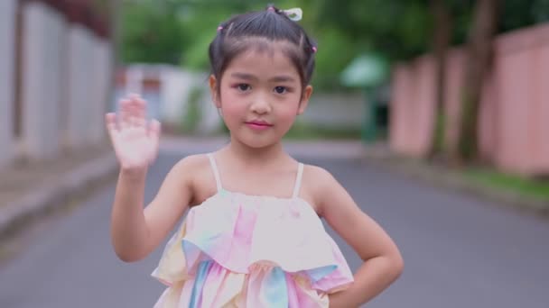 一个迷人的亚洲小女孩的画像 微笑着看着相机 挥挥挥手 开心地微笑着的孩子看着相机 特写镜头 快乐的自然童年休闲理念 — 图库视频影像