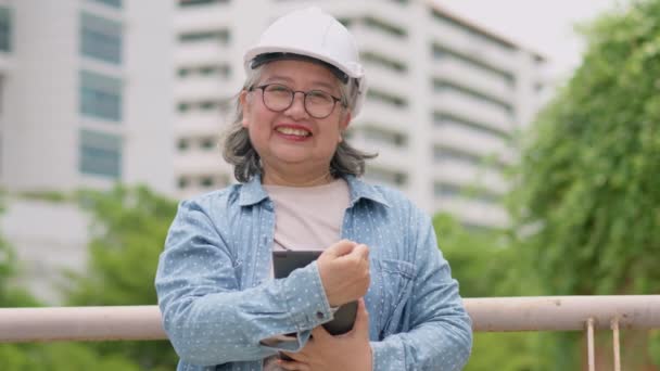 ポジティブな年齢のアジアの女性建築は タブレットを保持し 建設完了後に建物を検査するために市の前に立っています エンジニアリング 建設コンセプト — ストック動画