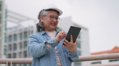 Hardhat tabletindeki Asyalı kadın mimari pozitiftir. İnşaat, Mühendislik ve inşaat konsepti tamamlandıktan sonra incelenmek üzere şehrin önünde durur..