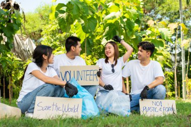 Mutlu Asyalı genç öğrenciler parkta temizlik için bir kampanya tabelası tutuyorlar, çevre koruma kavramı, geri dönüşüm, sürdürülebilirlik için yardım..