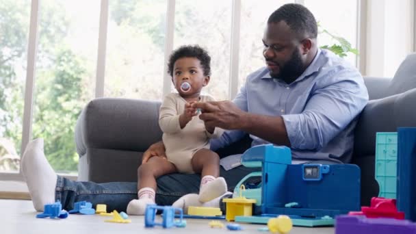 小さな幼児の子供と幸せなアフリカ系アメリカ人の男性がリビングルームのソファで遊んでいます 両親と子供は家でリラックスしています 両親と幼児の子供の女の子は家で過ごす時間を楽しんでいます — ストック動画