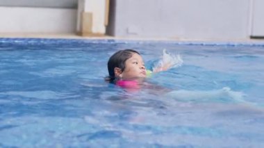 Neşeli Asyalı şirin kız mayo giyen tatlı kız su parkında mutlu bir gülümseme ile yüzme eğitimi almanın ve yaz okulunda egzersiz yapmanın keyfini çıkarıyor. Çocuk rahatla..