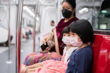 Cerrahi maskeli küçük kız, toplu taşımada (hava treni veya metro) koruma gribi ve virüs salgınıyla karşı karşıya. Yeni normal yaşam tarzı kavramı, okula gitmek için toplu taşıma araçlarını kullanmak..