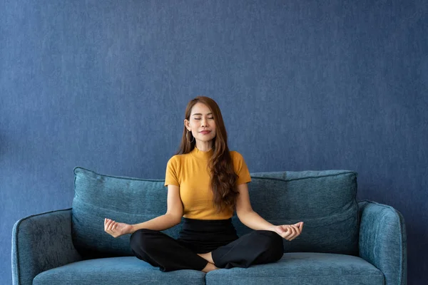 Portrait of healthy Asian woman meditating and exercise pose yoga on the sofa in morning. Zen relaxation and mindfulness lifestyle, Concept of indoor workout for good healthy and breathing practice.