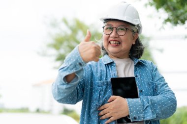 Mutlu Asyalı profesyonel mühendis miğfer takıyor ve inşaat alanındaki bir tabletin taslağını kontrol ediyor müteahhit ve mimar evi ve binayı yeniledikten sonra.