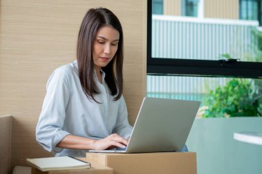 Mutlu Asyalı genç girişimci ev bilgisayarındaki bir dizüstü bilgisayardan siparişleri kontrol ettikten sonra satış başarısı için gülümseyin, İnternet ve e-ticaret ticaret sektörü kavramı