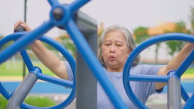 Kıdemli Asyalı kadın halka açık parktaki egzersiz istasyonlarında günlük antrenman yapıyor. Fiziksel aktivitelerle genç kalmayı, açık hava spor salonunu temsil ediyor. Fiziksel sağlık konsepti. Şehir parkında açık hava fitness ekipmanları