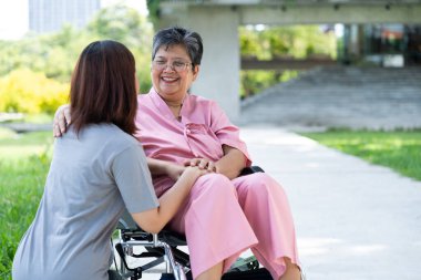 Tekerlekli sandalyedeki hastayla ilgilenen Asyalı dikkatli bir bakıcı ya da hemşire. Bakıcının, birikimin ve sağlık sigortasının özenle mutlu bir emeklilik kavramı hastayı teşvik eder.