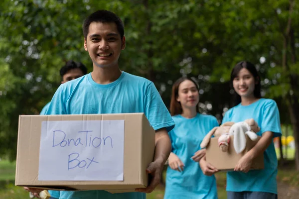 Happy young Asian students diverse volunteers hold donate box and toys for charity to share children and orphanages, a charity for sustainability. Volunteer work lifestyle and social cooperation
