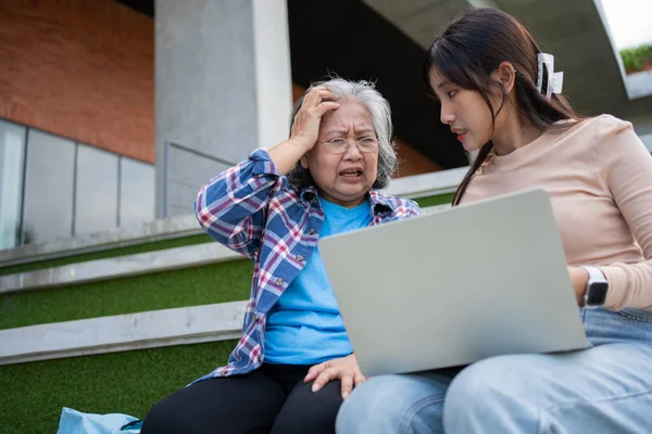 Asian daughter teaching old elderly woman use online Social media in computer laptop after retirement. Concept of Learning technology and adaptation of the elderly