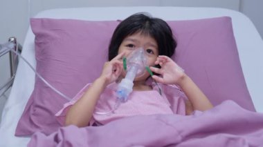 Küçük bir Asyalı kızın oksijen maskesi var ve hastanede nebulizatörle nefes alıyor. Bronşit konsepti, solunum ve tıbbi tedavi, nebulizatörden solunum ilacı, sis,.