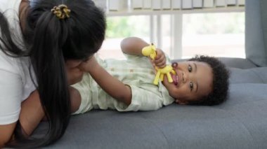 Mutlu Asyalı anne, küçük bebek bebekle oturma odasındaki kanepede oynuyor. Ebeveyn ve küçük çocuk evde dinleniyor. Ebeveynler ve küçük kız çocukları evde vakit geçirmekten zevk alıyorlar. Çocuk bakımı kavramı