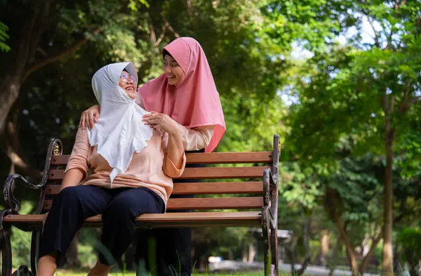 Hastane parkında hastayla ilgilenen Müslüman dikkatli bir bakıcı ya da hemşire. Mutlu Müslüman anne tesettüre sarılmış kız çocuğu. Tasarruf ve Kıdemli Sağlık Sigortası kavramı, Mutlu Bir Aile