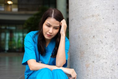 Stresli ve çok çalışan kadın doktor doktor cerrahın portresi hastanedeki ameliyathanenin yanında oturuyor ve maskeyi çıkarıyor.