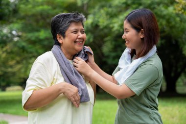 Parkta sabah egzersizinde birlikte çalışan çekici bir anne ve kız çocuğu. Kız, annesinin terini beyaz havluyla, yaşlı bir bakıcı ve mutlu bir aile kavramı ile emiyor..