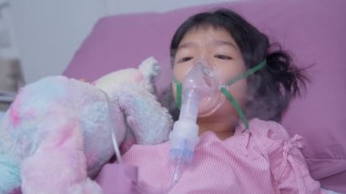 Küçük bir Asyalı kızın oksijen maskesi var ve hastanede nebulizatörle nefes alıyor. Bronşit konsepti, solunum ve tıbbi tedavi, nebulizatörden solunum ilacı, sis,.