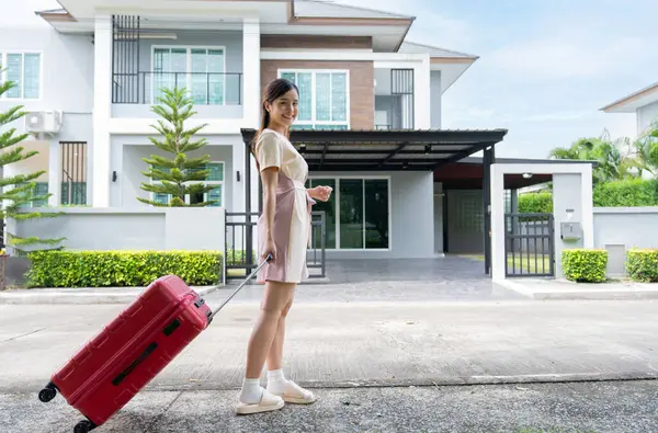 A young Asian woman with luggage standing in front of a new buying home to move into a new house. Start life at own or rented flat concept and Moving Day concept.