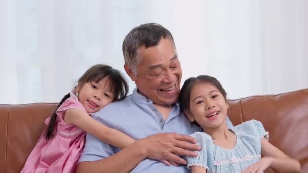 ハッピーアジアのシニアの祖父は孫娘とソファーに座り 自宅のリビングルームで孫娘と遊びます 家族のコンセプトは彼らの家で楽しんでいます — ストック動画