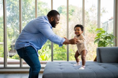 Mutlu Afrikalı Amerikalı Baba 'nın portresi. Evdeki kanepede küçük tatlı bir bebekle oturuyor. Babası gülümsüyor ve kızını eğlendiriyor.