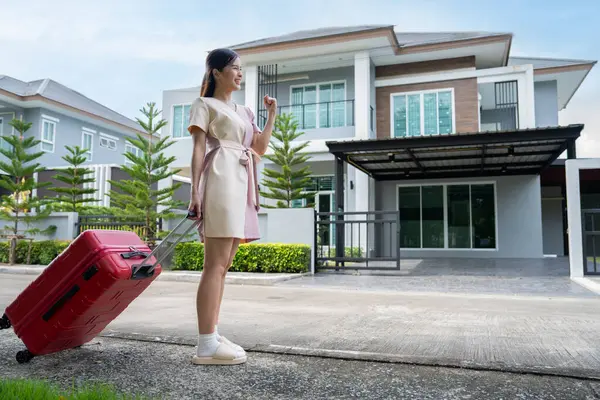 A young Asian woman with luggage standing in front of a new buying home to move into a new house. Start life at own or rented flat concept and Moving Day concept.